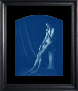 Seated nude figure in blue-toned photograph.