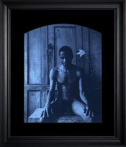 Seated person with flower in background.